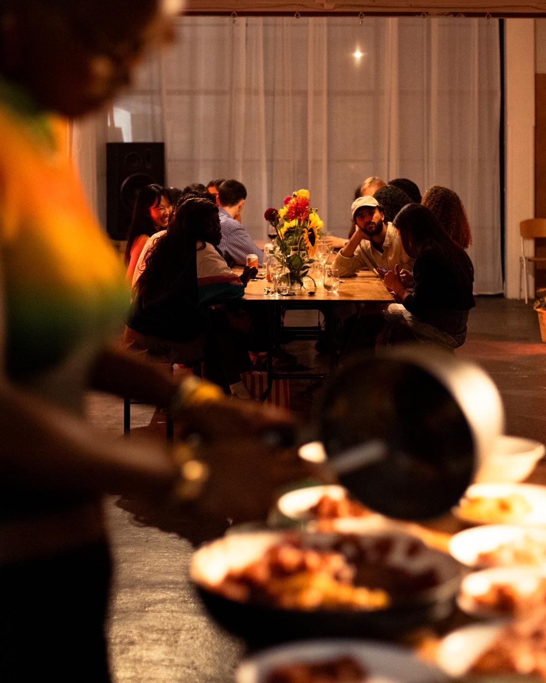 Food being served at a supper club with guests at a long table behind